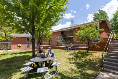 Students working at a picnic table outside Campus Heights residence hall in the shade of a tree.