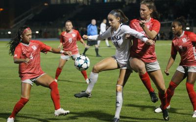 An NAU Soccer match where the NAU athlete has control over the ball but is surrounded on all sides by her opponents.
