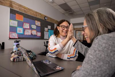 A student and professor look at a laptop and high-five.