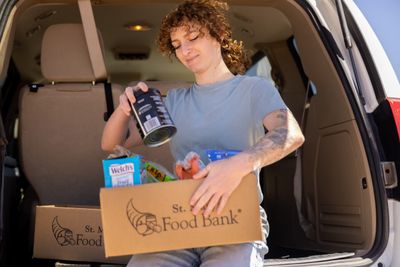 A Food Bank volunteer adds cans of food to a box.