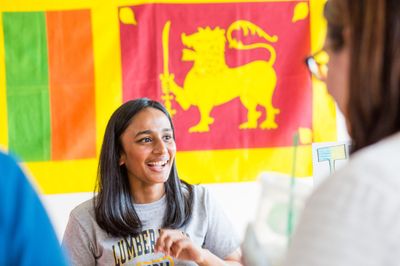 Student with a "Lumberjack" tee shirt is smiling and standing in front of a group of international flags.