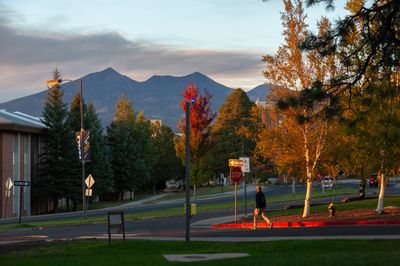 A student walking on the NAU campus, surrounded by beautiful fall tree colors.